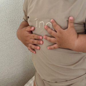 Child in a Ina Rash Shirt - Sand Colour with hands on chest, close-up view.