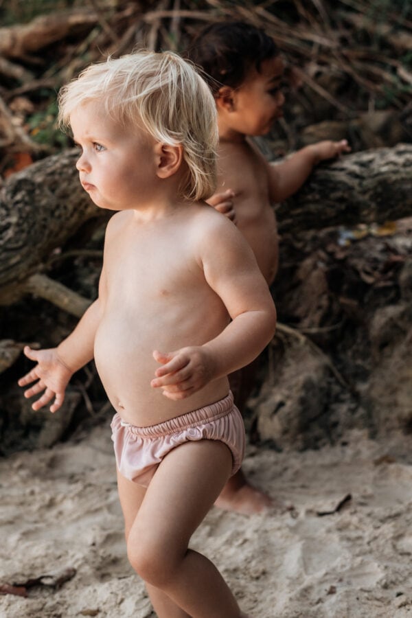 Two children standing on the sand next to a Lumi Brief Swim Nappy.