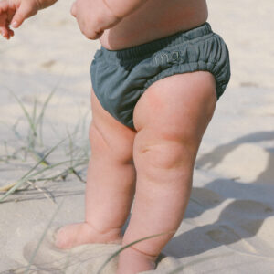A baby standing in the sand wearing a Lumi Brief Swim Nappy.