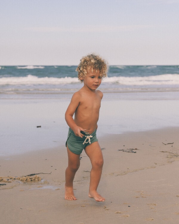 A young boy wearing Mesa Trunks running on the beach.