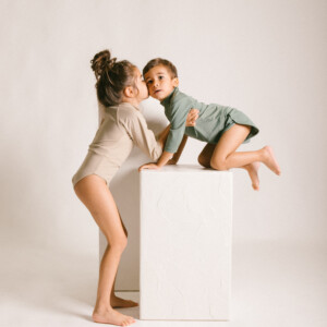 Two children kissing on the June Long Sleeve One-Piece in a studio.