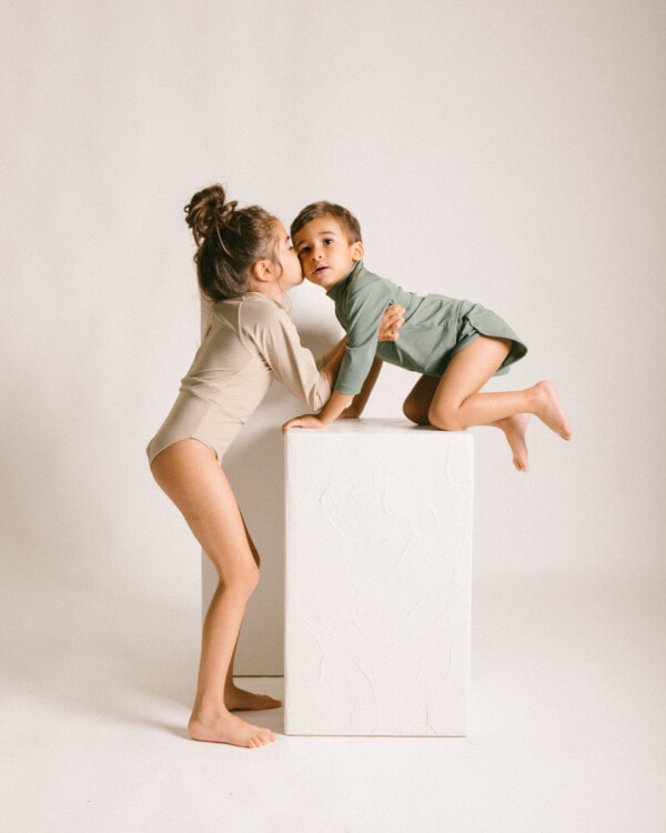 Two children kissing on the June Long Sleeve One-Piece in a studio.