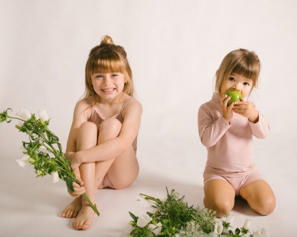 Two little girls sitting on a white background with Lumi Short Swim Nappy.