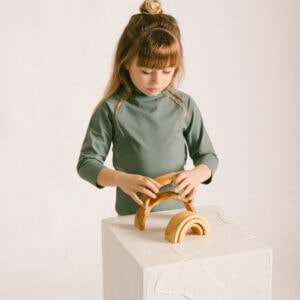 A young girl focusing intently on assembling a Nella Rash Shirt - Moss Colour.