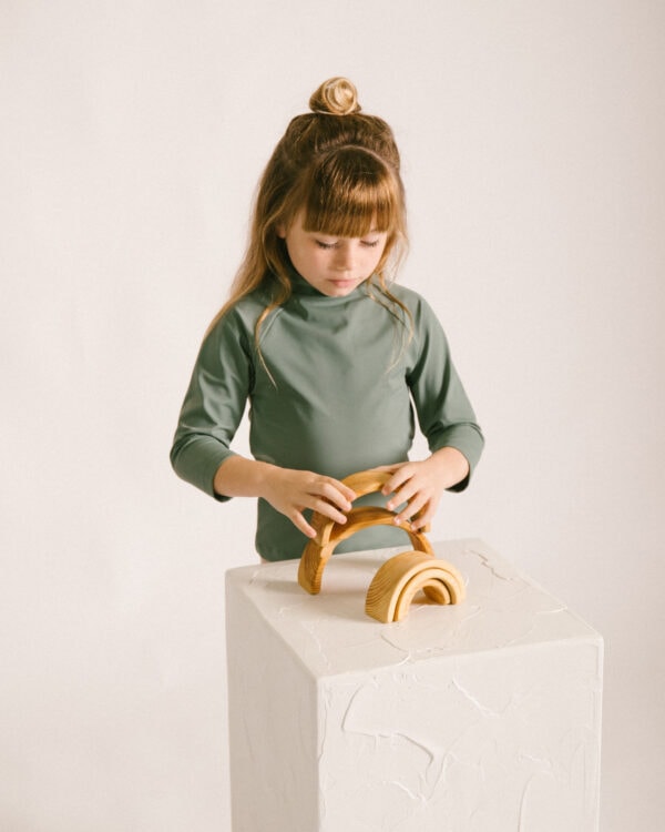 A young girl focusing intently on assembling a Nella Rash Shirt - Moss Colour.