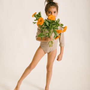 A young girl holding a bouquet of June Long Sleeve One-Piece orange flowers.