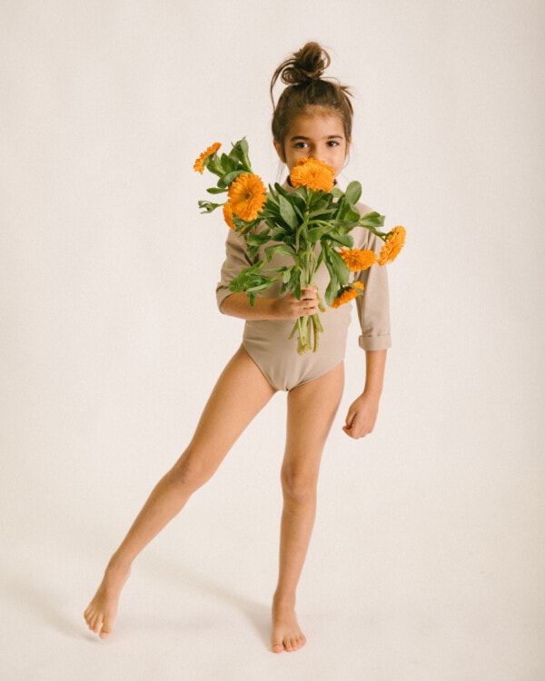 A young girl holding a bouquet of June Long Sleeve One-Piece orange flowers.
