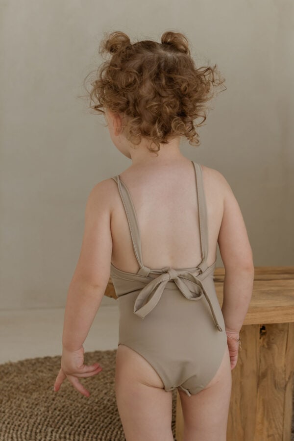 The back of a child wearing the Essentials Range - Mara One-Piece - Sand Colour swimsuit.