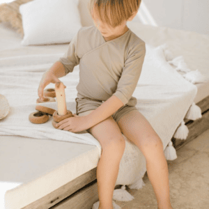A young boy playing with an Ada Rash Shirt on a bed.