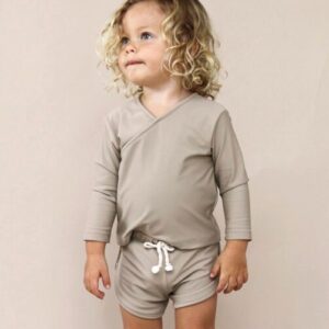 Toddler with curly hair standing in an Ada Rash Shirt - Sand Colour.