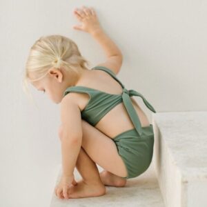 Toddler in an Arla Bikini - Moss Colour sitting on the edge of a step.
