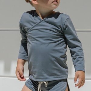 A young boy wearing the Essentials Range - Ada Rash Shirt in Mineral Colour and shorts.