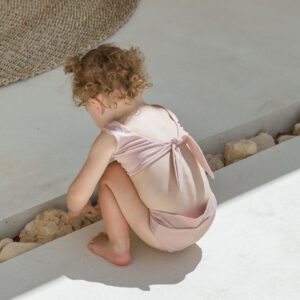 A little girl in the Essentials Range - Arla Bikini - Rose Colour sitting on the ground.