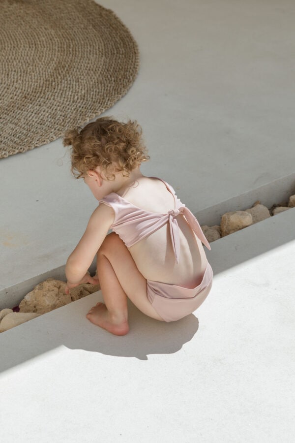 A little girl in the Essentials Range - Arla Bikini - Rose Colour sitting on the ground.