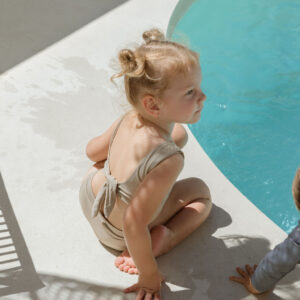 Two children sitting on the edge of a pool wearing Arla Bikini - Sand Colour from the Essentials Range.