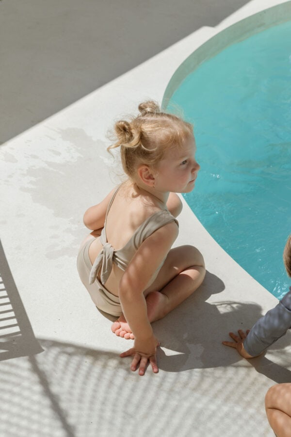 Two children sitting on the edge of a pool wearing Arla Bikini - Sand Colour from the Essentials Range.