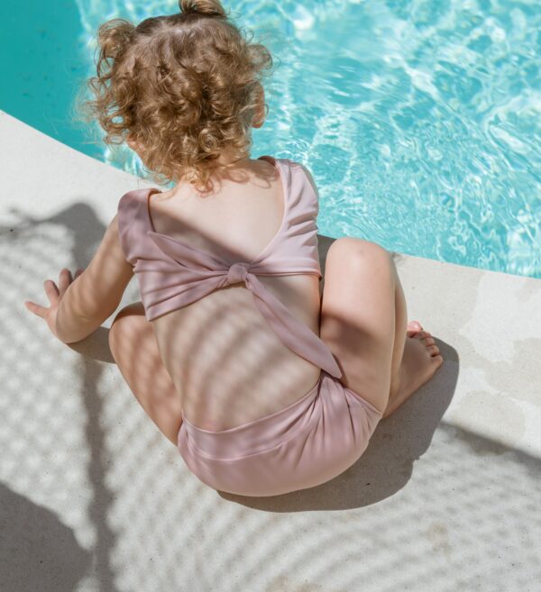 A little girl in the Essentials Range - Arla Bikini - Rose Colour sitting on the edge of a pool.