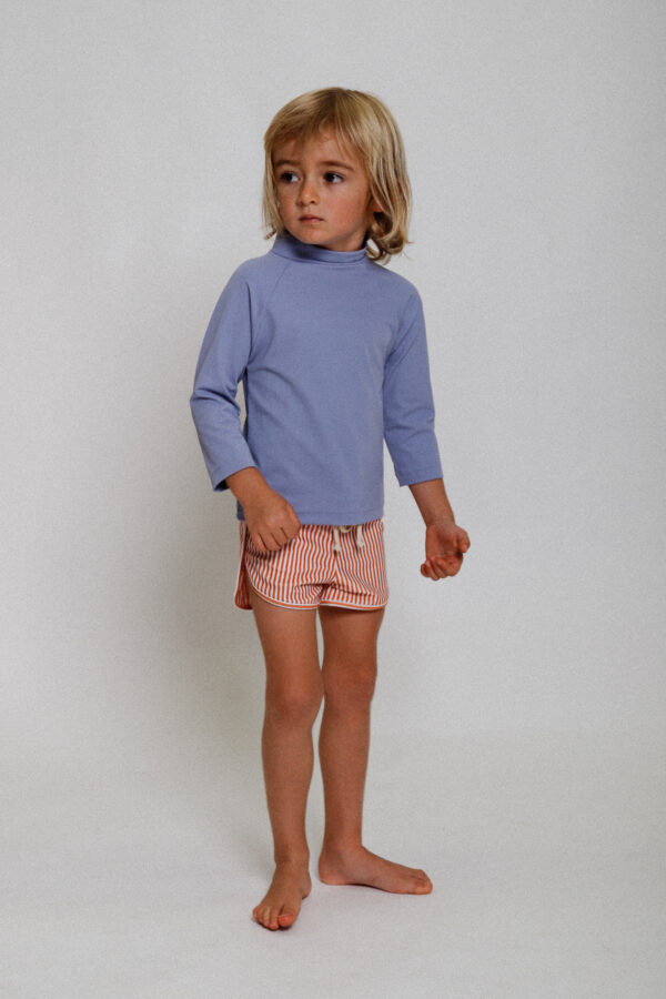 A young boy in a Playtime Collection - Nella Rash Shirt - Mandarin and pink shorts.
