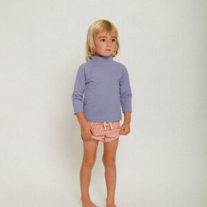 A little girl wearing a Playtime Collection - Nella Rash Shirt - Mandarin and pink shorts.