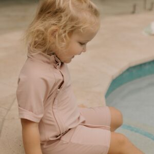 Young girl sitting beside a pool in a Zimmi Onesie - Rose.