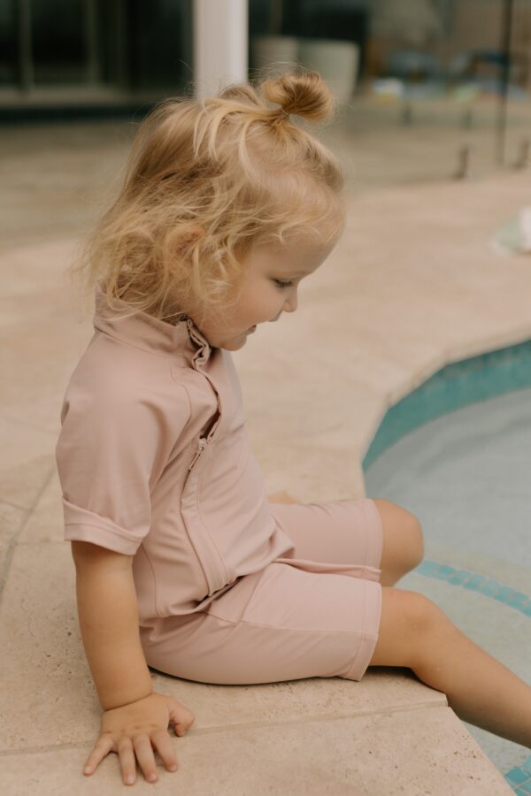Young girl sitting beside a pool in a Zimmi Onesie - Rose.