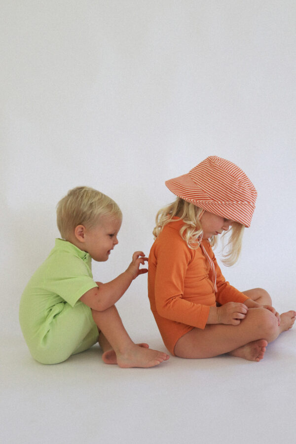 Two children sitting on the floor with a Playtime Collection - Lumi Brief Swim Nappy - Mandarin on.