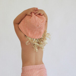 A little girl wearing a Playtime Collection - Lumi Brief Swim Nappy - Mandarin and shorts.