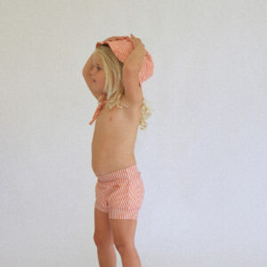 A little girl wearing the Playtime Collection - Lumi Brief Swim Nappy - Mandarin hat and shorts.