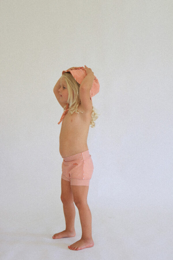 A little girl wearing the Playtime Collection - Lumi Brief Swim Nappy - Mandarin hat and shorts.