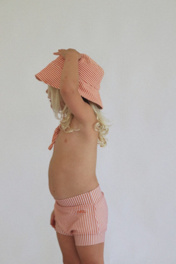 A little girl wearing the Playtime Collection - Lumi Brief Swim Nappy - Mandarin and shorts.