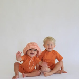 Two small children wearing Playtime Collection - Lumi Brief Swim Nappy - Mandarin rompers and hats.