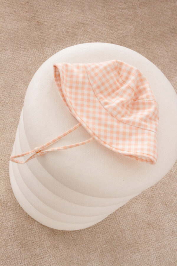 A Unisex Vali Bucket Hat - Apricot Gingham on a pillow.