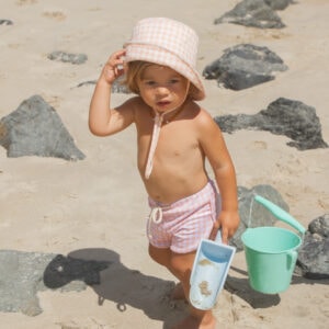 A little girl holding the Azure and Apricot Gingham - Mesa Trunks on the beach.