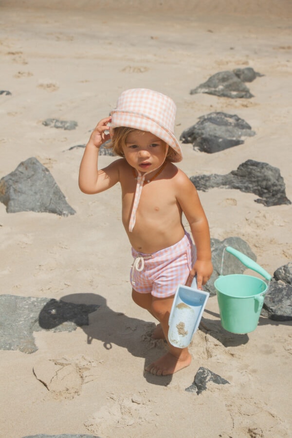 A little girl holding the Azure and Apricot Gingham - Mesa Trunks on the beach.