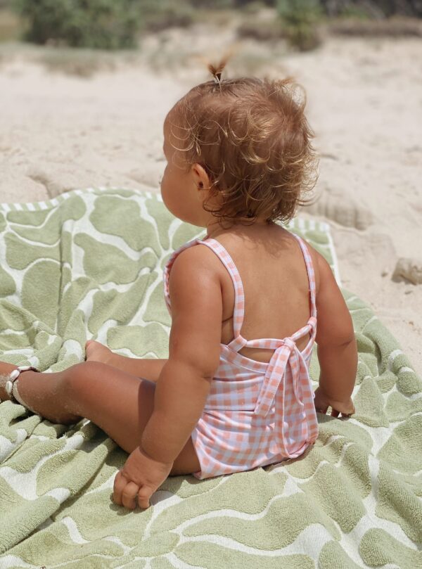 A baby sitting on a Mara One-Piece - Apricot Gingham towel on the beach.