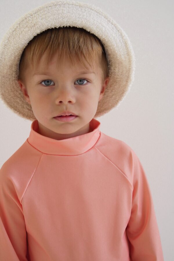 A young boy wearing a hat and a Sorbet Summer - Nella Rash Shirt.