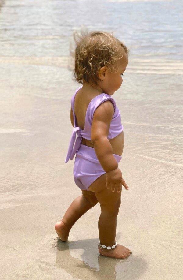 A baby girl in a Sorbet Summer - Arla Bikini - Grape Colour walking on the beach.