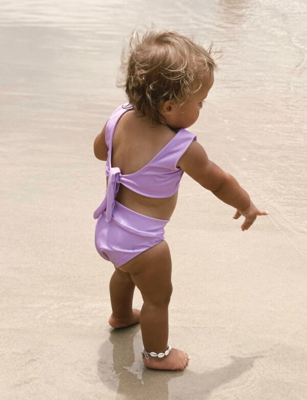 A baby girl in a Sorbet Summer - Arla Bikini - Grape Colour standing on the beach.