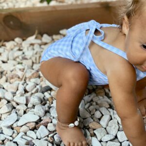 A baby crawling on rocks in a Mara One-Piece - Azure Gingham swimsuit.