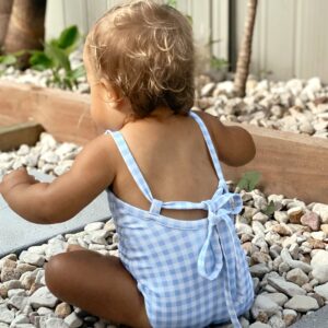 A baby in a Mara One-Piece - Azure Gingham swimsuit sitting on rocks.