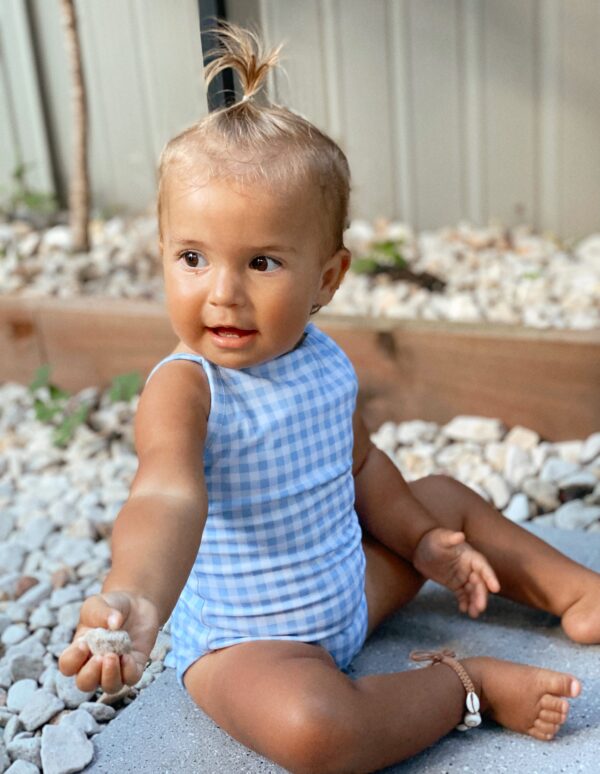 A baby girl wearing the Mara One-Piece - Azure Gingham.