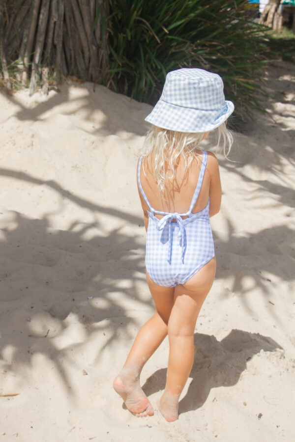 A little girl wearing the Azure & Apricot Gingham - Mara One-Piece swimsuit and hat.