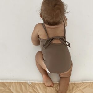 A baby in the Essentials Range - Mara One-Piece - Tort Colour swimsuit on a white mat.
