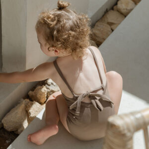 A little girl wearing an Essentials Range - Mara One-Piece - Tort Colour sitting on the steps of a house.