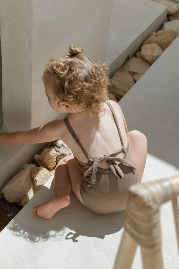 A little girl wearing an Essentials Range - Mara One-Piece - Tort Colour sitting on the steps of a house.