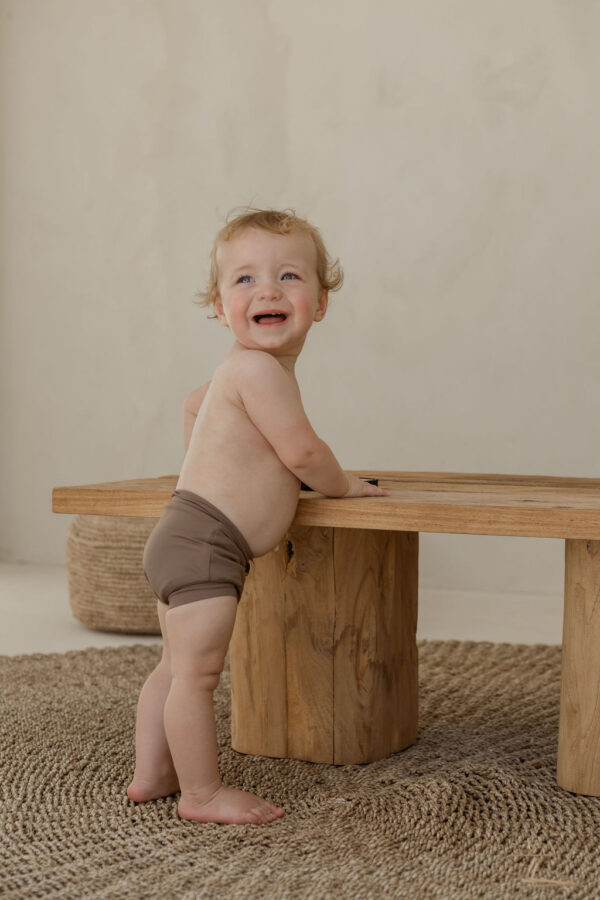 A baby standing on top of a Essentials Range - Lumi Short Swim Nappy - Tort Colour.