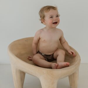 A baby is sitting in a Essentials Range - Lumi Brief Swim Nappy - Tort Colour chair.