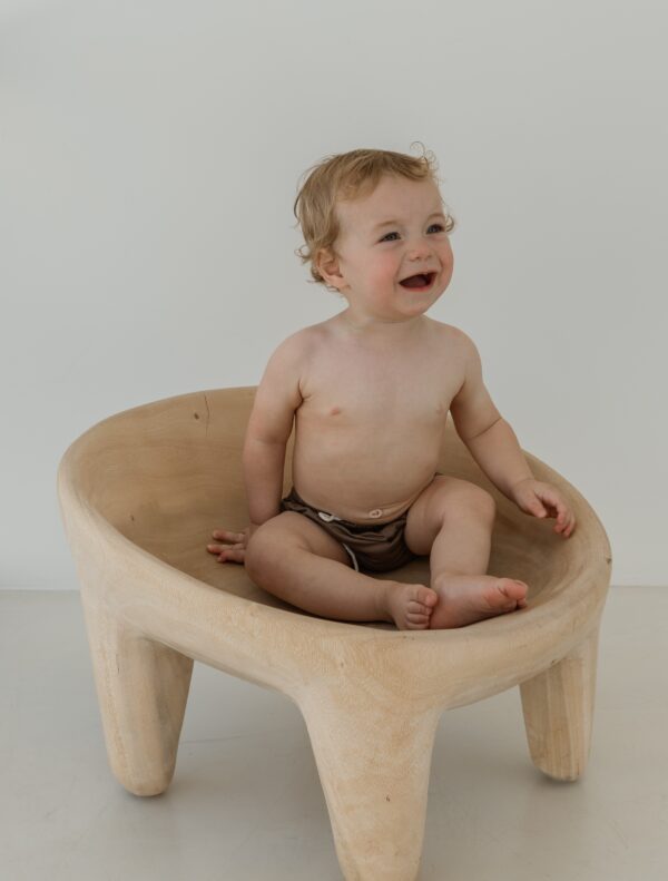A baby is sitting in a Essentials Range - Lumi Brief Swim Nappy - Tort Colour chair.