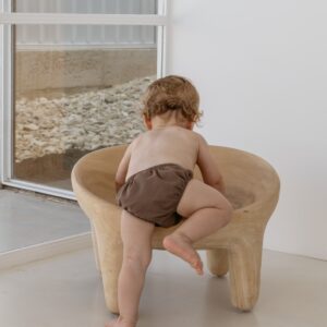 A baby sitting on a Essentials Range - Lumi Brief Swim Nappy - Tort Colour in a room.