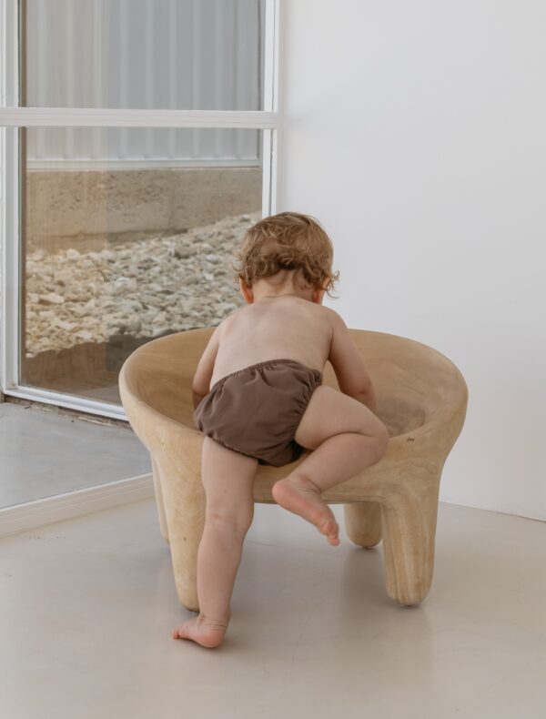 A baby sitting on a Essentials Range - Lumi Brief Swim Nappy - Tort Colour in a room.